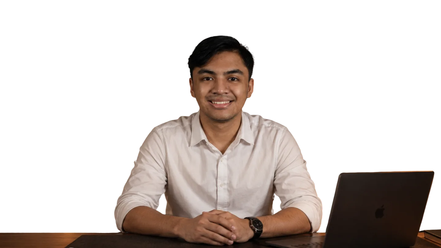 Arif Kamil at his desk in a warm lamp-lit room, hands folded, smiling